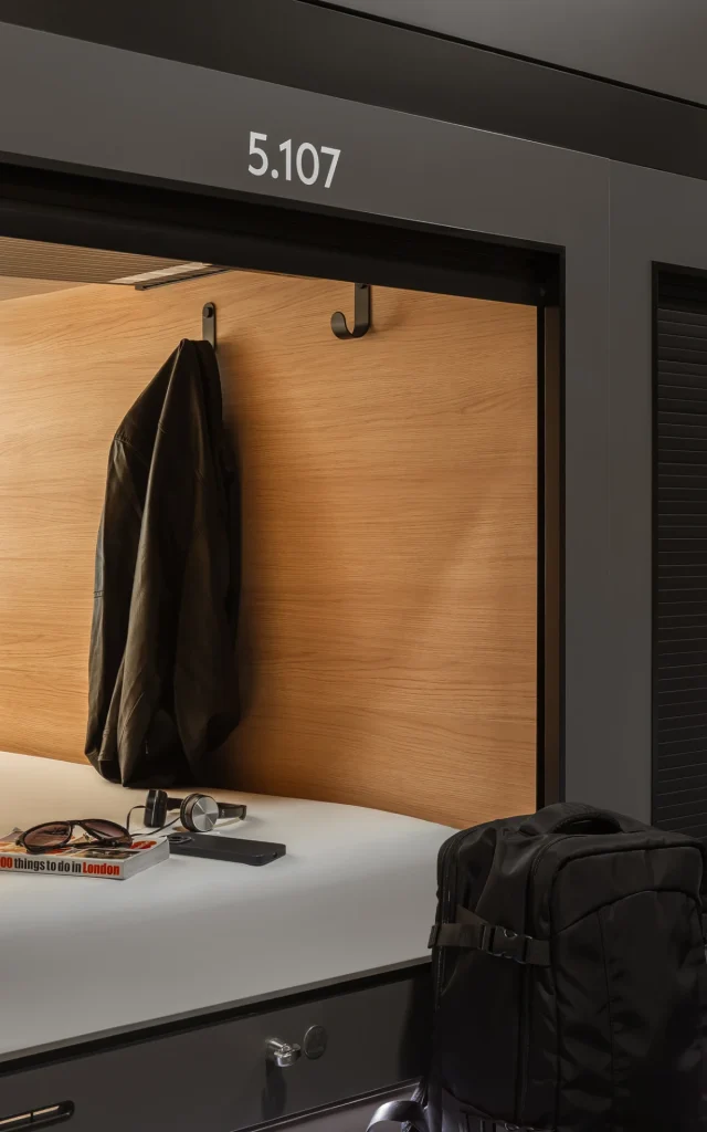 A Capsule with a jacket, small backpack and books on the bed